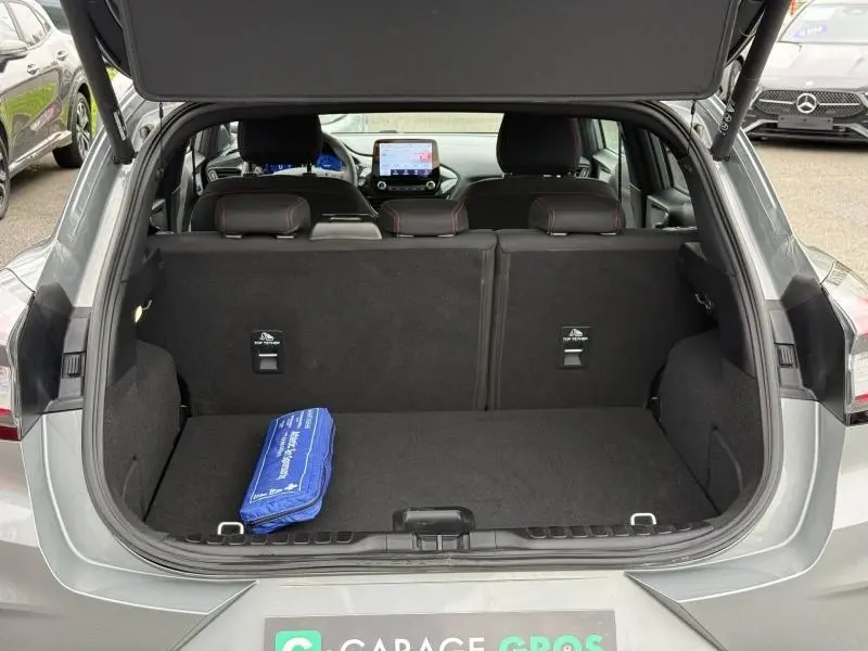 Vue arrière du coffre ouvert d'un Ford Puma gris 2024, montrant l'intérieur spacieux et la tablette tactile du tableau de bord.