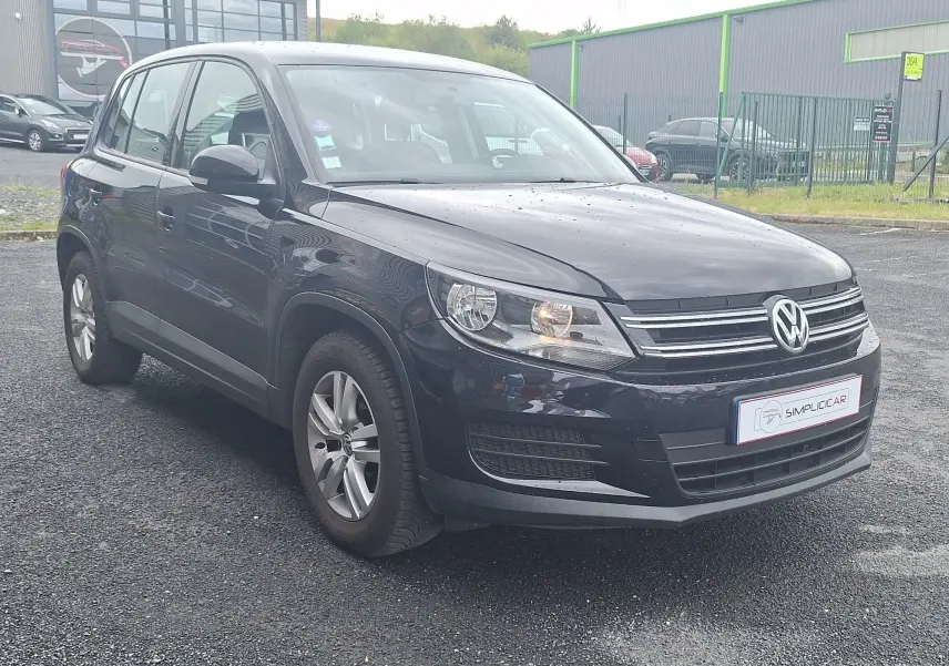 Volkswagen Tiguan noir 2014 en 3/4 avant droit, avec jantes alliage 16 pouces et phares allumés.
