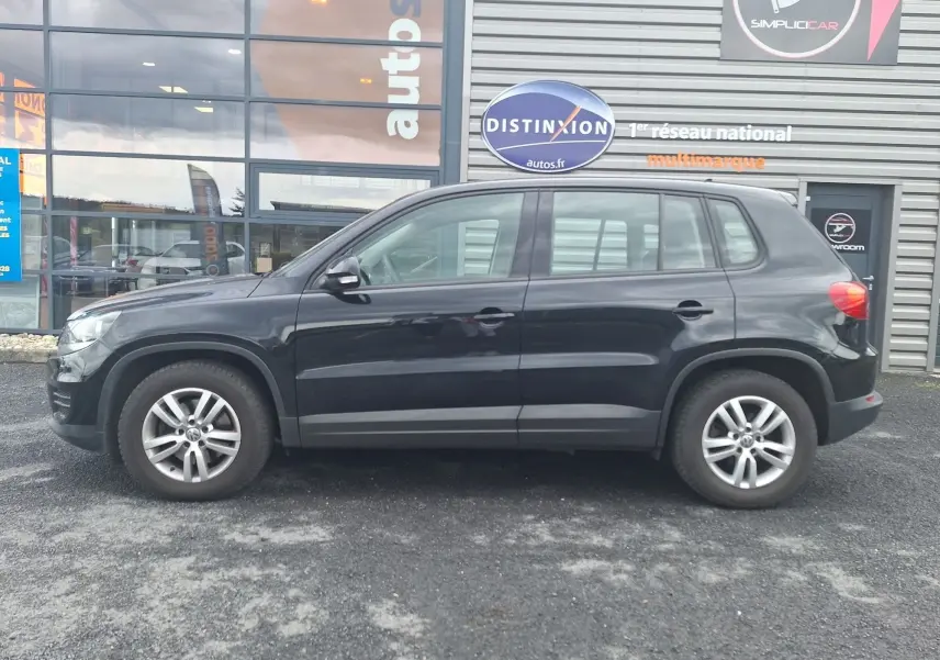 Profil côté gauche d'un Volkswagen Tiguan noir 2014 avec jantes alliage 16 pouces, garé devant un bâtiment commercial.