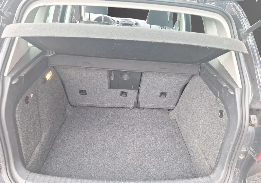 Coffre ouvert d’un Volkswagen Tiguan noir 2014, vue arrière montrant l’espace de chargement et la tablette cache-bagages relevée.