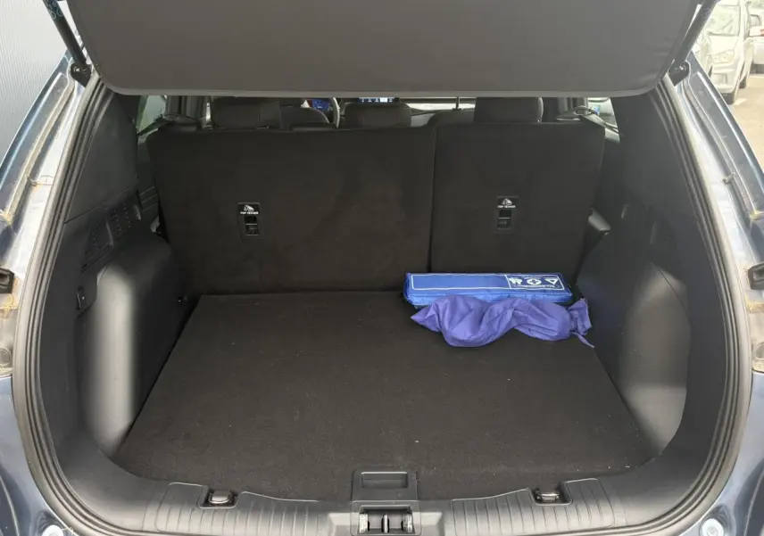 Coffre ouvert d’un Ford Kuga bleu azur 2023, vue arrière montrant un espace de chargement propre avec un kit de sécurité.