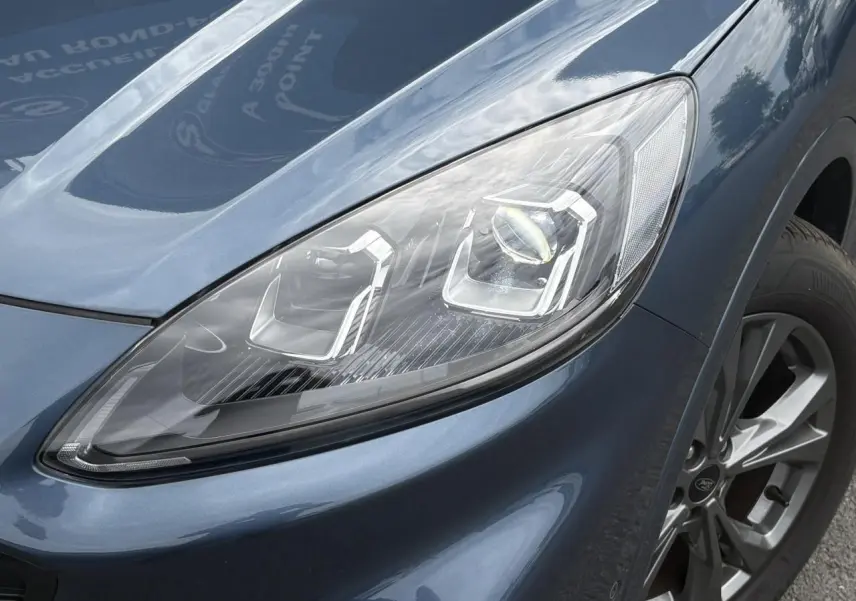 Gros plan sur le phare avant droit et la jante alliage 18 pouces du Ford Kuga Bleu Azur 2023 finition ST-Line.