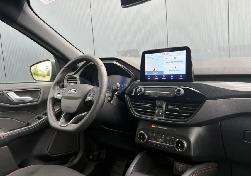 Vue intérieure côté conducteur du Ford Kuga 2023, tableau de bord noir avec écran tactile et volant ST-Line à surpiqûres rouges.