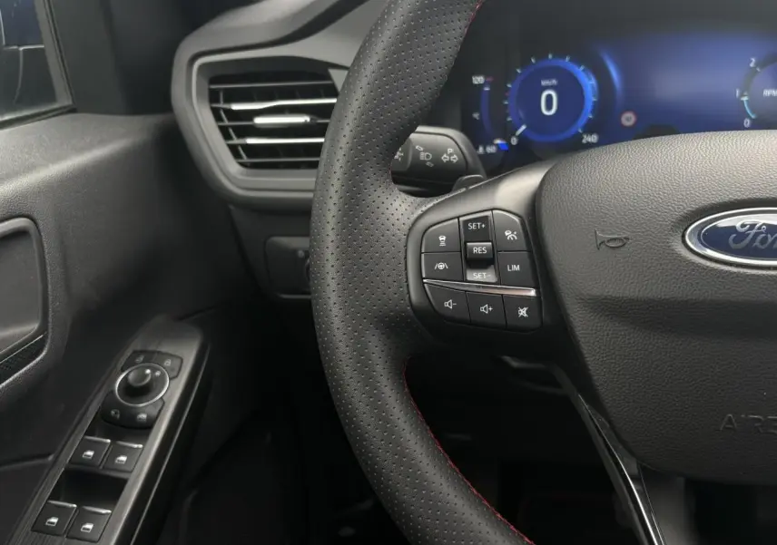 Gros plan sur le volant perforé noir avec surpiqûres rouges et tableau de bord numérique bleu du Ford Kuga 2023.