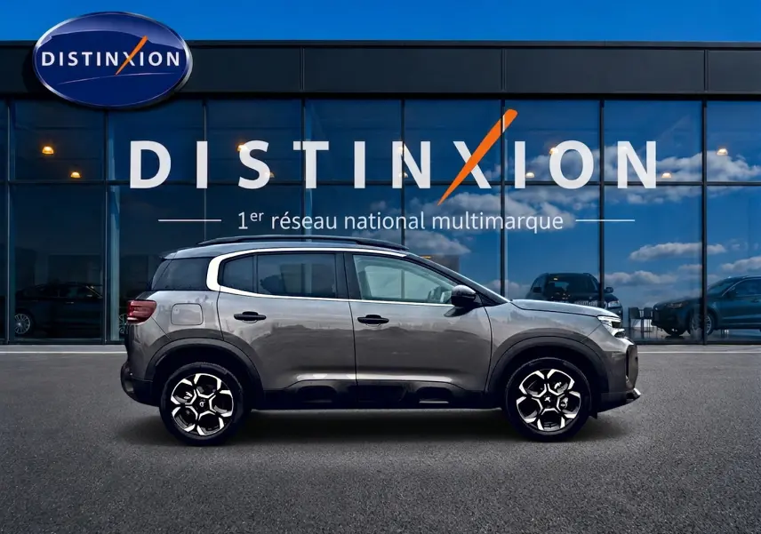Profil droit du Citroën C5 Aircross gris platinium 2025, avec jantes alu et barres de toit visibles devant vitrine Distinxion.