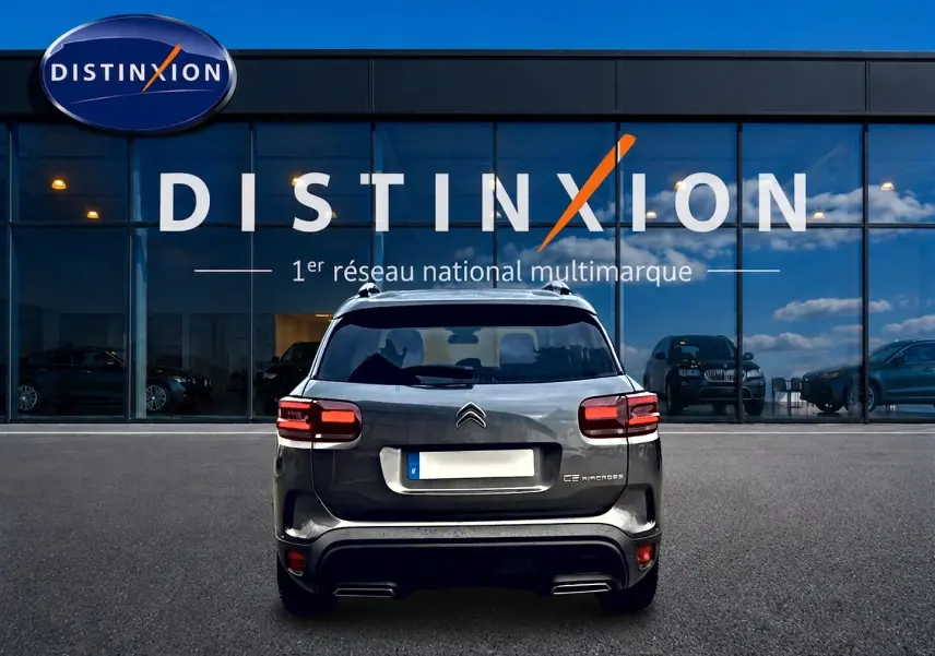 Vue arrière d'un Citroën C5 Aircross gris platinium garé devant une vitrine avec logo Distinxion.