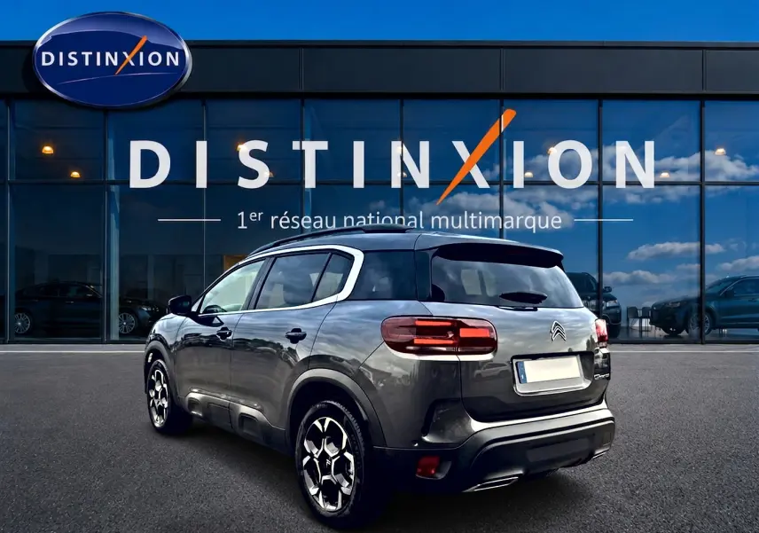 Citroën C5 Aircross gris platinium vue 3/4 arrière droit, avec jantes alu et barres de toit visibles.