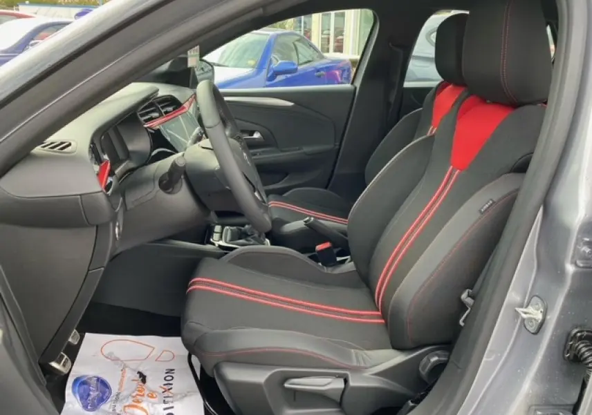 Vue intérieure côté conducteur de l'Opel Corsa gris magnetic 2022, sièges tissu noir et rouge avec surpiqûres rouges.