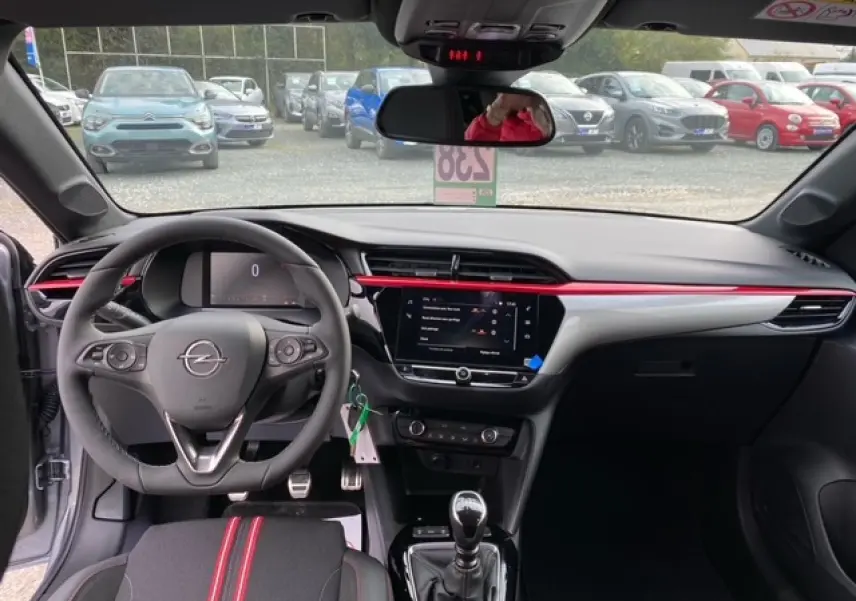 Intérieur avant de l’Opel Corsa gris Magnetic 2022, volant multifonction, tableau de bord noir avec bande rouge et écran tactile central.