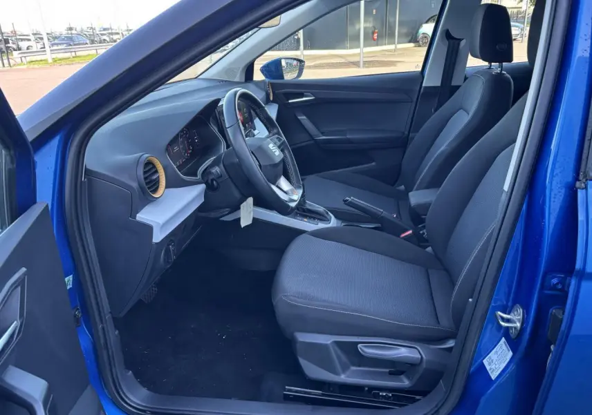 Vue intérieure côté conducteur d'une SEAT Arona bleu saphir 2024 avec sièges tissu et volant multifonction cuir.