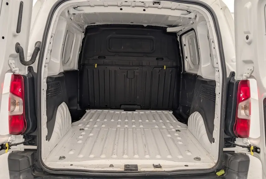 Vue arrière du Citroën Berlingo Fourgon blanc Banquise montrant l'espace de chargement vide avec cloison noire et feux arrière allumés.