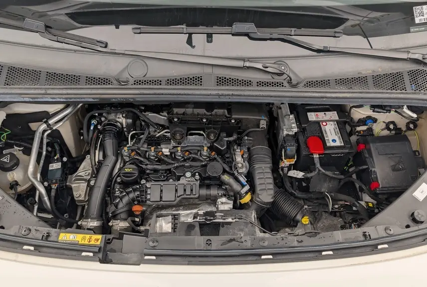 Vue plongeante sur le moteur diesel du Citroën Berlingo Van blanc banquise, montrant les composants sous le capot ouvert.