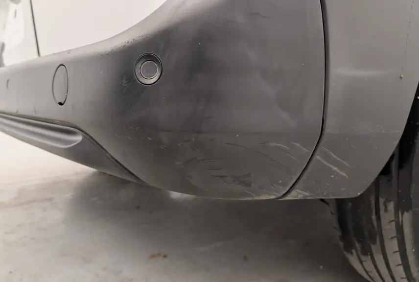 Gros plan sur le pare-chocs arrière droit noir du Citroën Berlingo Van blanc, montrant le capteur de recul et la roue.