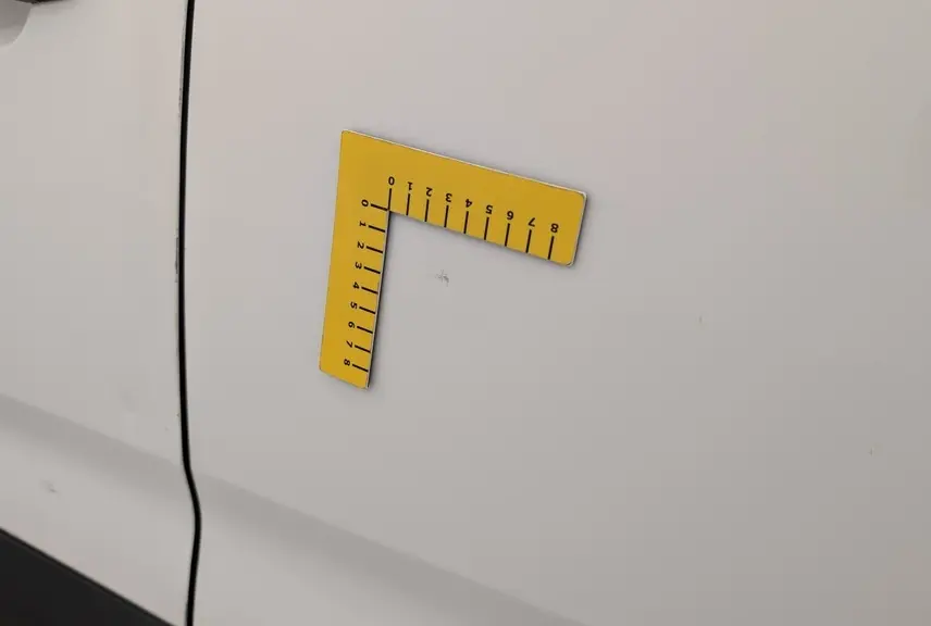 Détail de la porte latérale droite blanche Banquise du Citroën Berlingo Fourgon 2020 avec petite éraflure mesurée par un gabarit jaune.