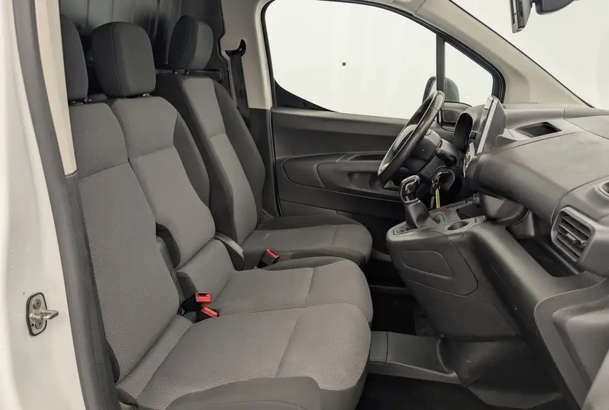 Vue intérieure côté conducteur du Citroën Berlingo Van blanc, montrant les sièges tissu gris et le tableau de bord avec écran tactile.