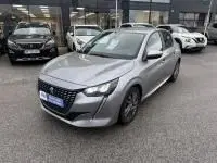 Peugeot 208 1.2 PureTech 100 Style gris en 3/4 avant droit, avec calandre noire et phares LED, stationnée en extérieur.