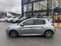 Peugeot 208 1.2 PureTech 100 Style gris vue de profil côté gauche, garée devant un concessionnaire automobile.