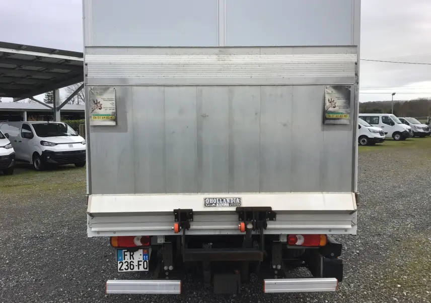 Vue arrière d’un Opel Movano blanc avec hayon électrique et caisse fermée, stationné sur un sol gravillonné.