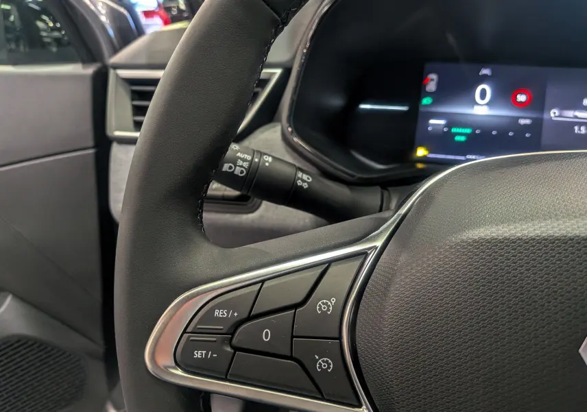 Gros plan sur le volant côté gauche de la Renault Clio V gris schiste, avec commandes de régulateur et tableau de bord numérique.