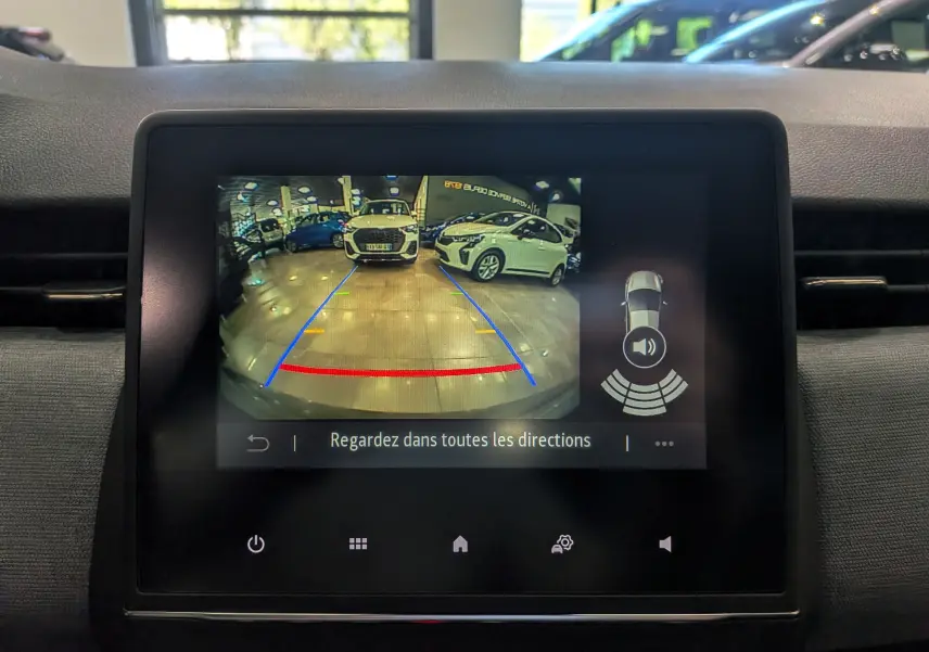 Écran central montrant la caméra de recul avec vue arrière sur un parking intérieur et lignes de guidage colorées.