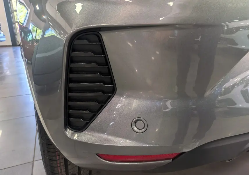 Gros plan sur l'angle arrière gauche de la Renault Clio V gris schiste, montrant la grille d'aération et le capteur de recul.
