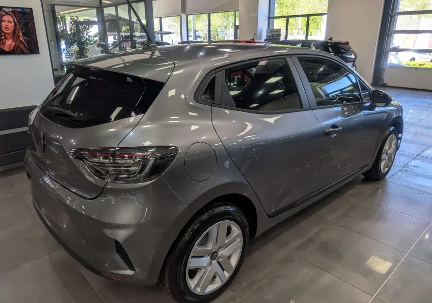 Vue 3/4 arrière droite d'une Renault Clio V gris schiste exposée en showroom, mettant en valeur ses feux arrière et jantes modernes.