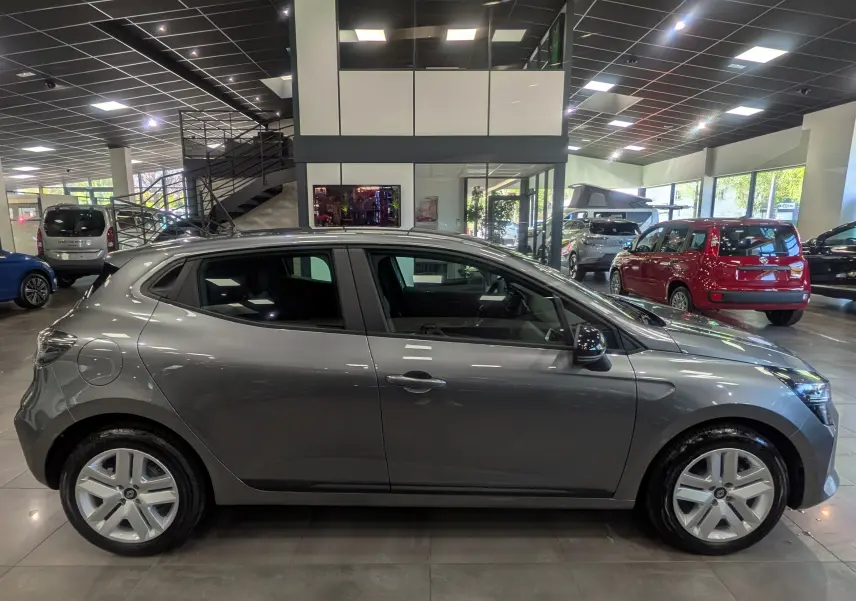 Profil côté gauche d'une Renault Clio V gris schiste 2025 en intérieur, avec jantes alliage et rétroviseurs noirs.