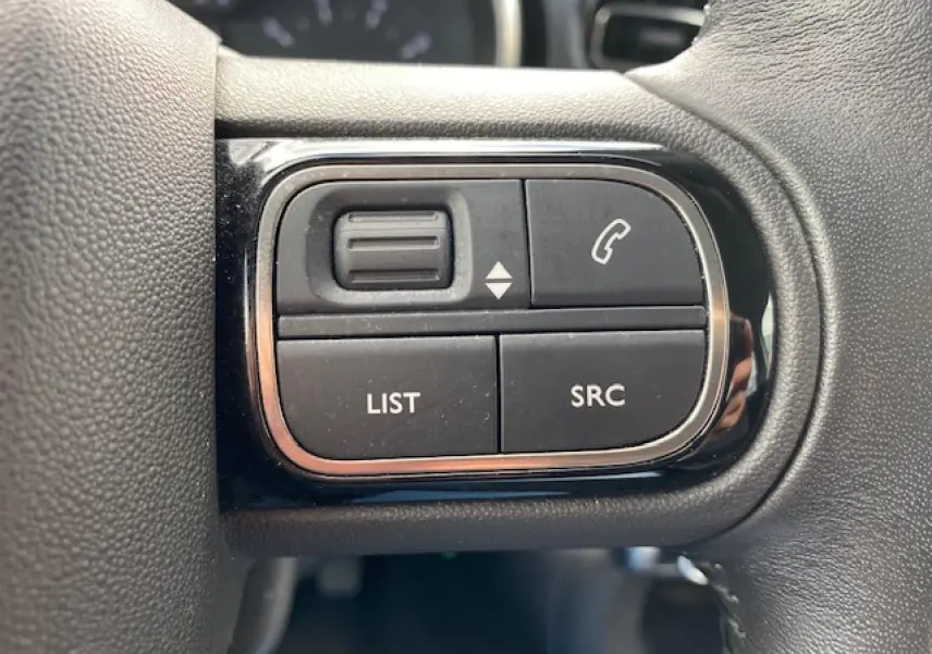 Gros plan sur les commandes au volant noir de la Citroën C3 gris clair, boutons d'appel et navigation audio visibles.