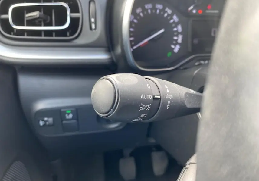 Gros plan sur la commande des phares automatiques à gauche du volant dans l'habitacle d'une Citroën C3 gris clair.