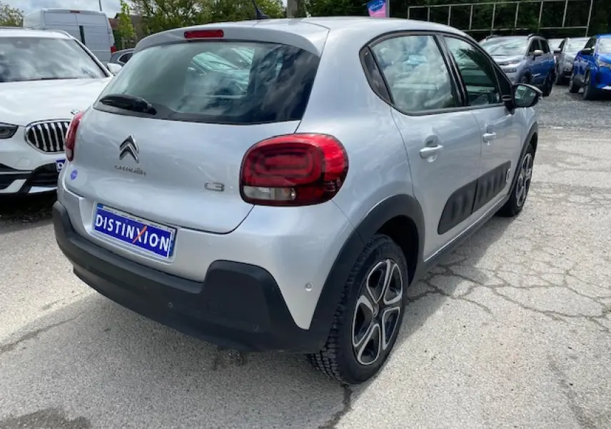 Vue 3/4 arrière droite d'une Citroën C3 gris clair avec enjoliveurs 3D et protections latérales noires.
