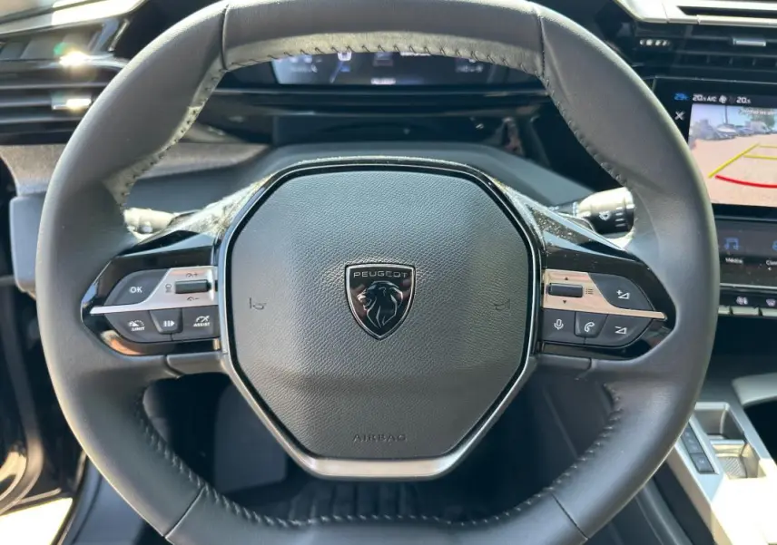 Vue rapprochée du volant noir du Peugeot 308 SW Hybrid 145 e-DCS6 Allure 2025 avec commandes intégrées et logo central.