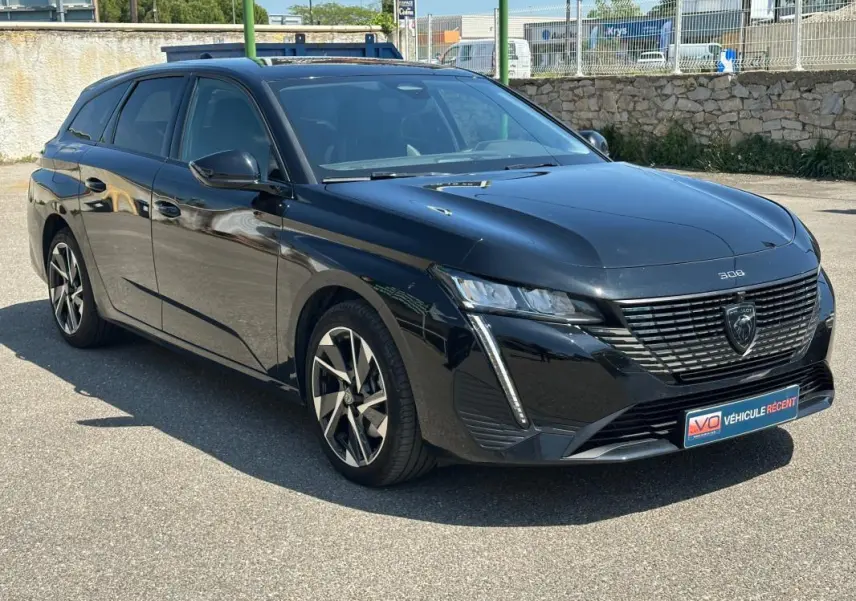 Peugeot 308 SW Hybrid 145 Allure noir vue 3/4 avant droit, avec calandre distinctive et feux LED verticaux.