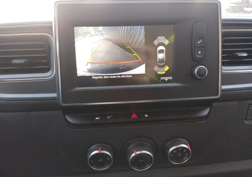 Vue intérieure centrée sur l'écran tactile du tableau de bord du Renault Master blanc, affichant la caméra de recul et les commandes de climatisation.