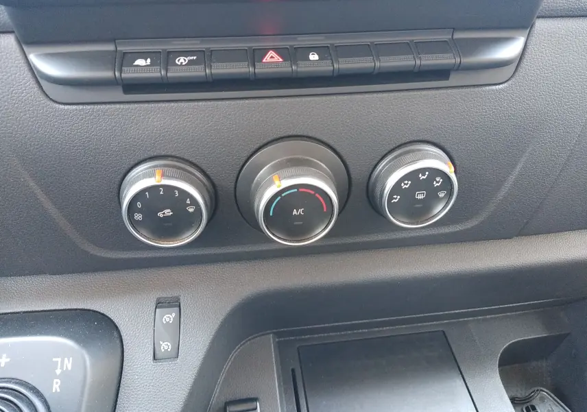 Gros plan sur les commandes de climatisation et les boutons de fonction du tableau de bord du Renault Master III blanc de 2020.