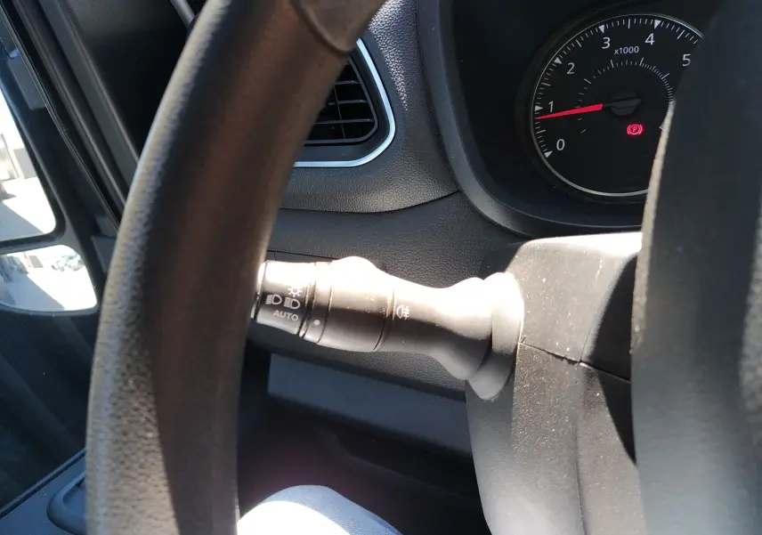 Vue intérieure rapprochée du commodo d'éclairage à gauche du volant du Renault Master blanc, avec compte-tours en arrière-plan.