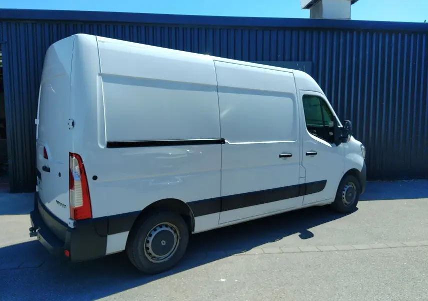 Renault Master blanc vu en 3/4 arrière droit, fourgon utilitaire avec porte latérale coulissante et attelage.