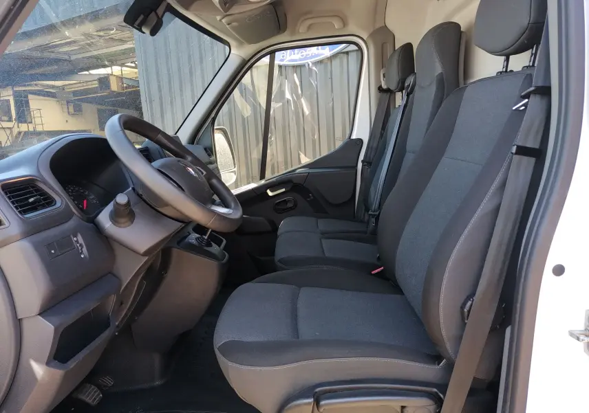 Intérieur du Renault Master III blanc, vue côté gauche montrant le poste de conduite et les trois sièges en tissu noir.