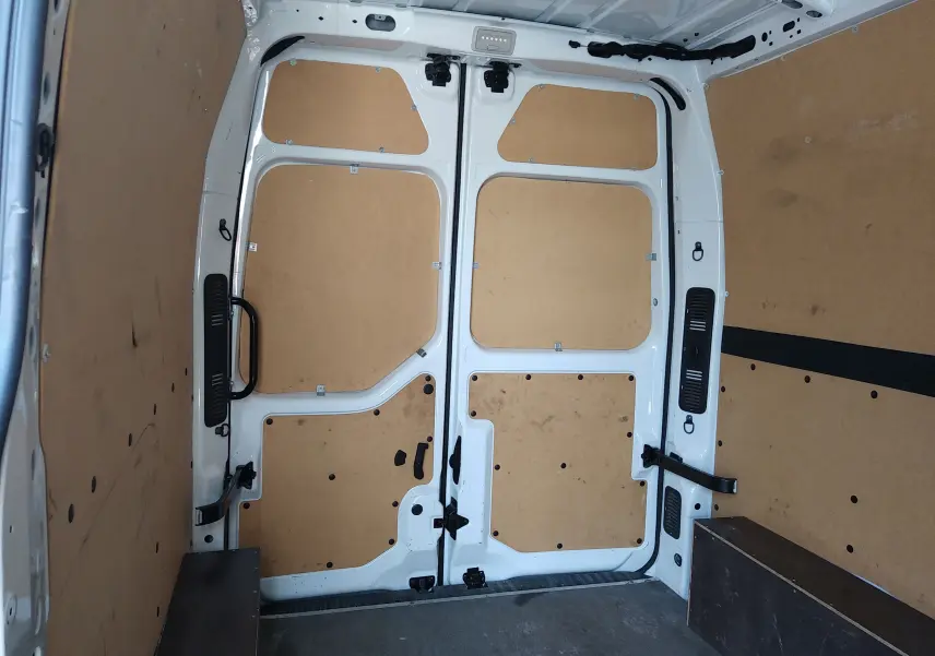 Intérieur du coffre d’un Renault Master blanc, vue arrière montrant les portes ouvertes avec habillage bois clair.