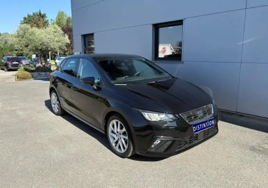 SEAT Ibiza 1.0 TSI 95 FR noire vue en 3/4 avant, stationnée devant un bâtiment gris par temps ensoleillé.