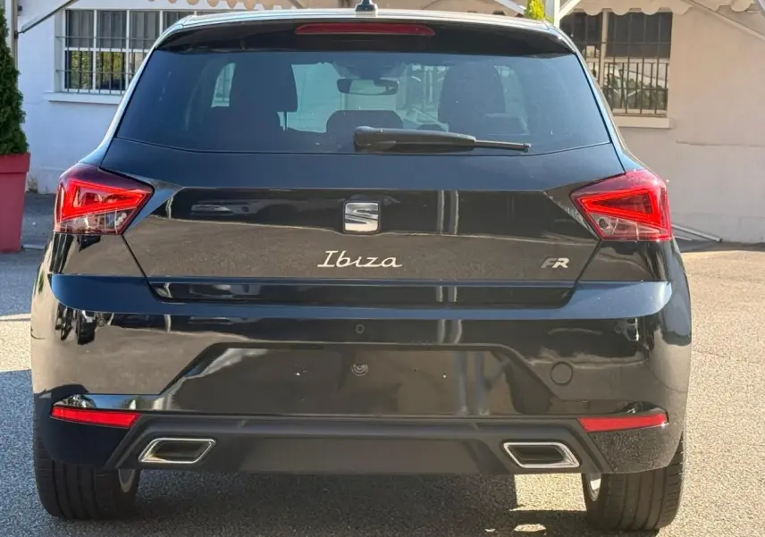 Vue 3/4 arrière droite d'une SEAT Ibiza noire 2025 avec feux LED et double sortie d'échappement chromée.