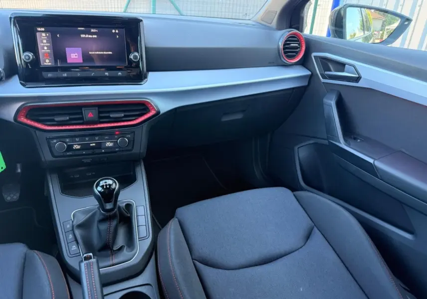 Intérieur avant droit de la SEAT Ibiza noire, tableau de bord avec écran tactile et détails rouges autour des aérateurs.