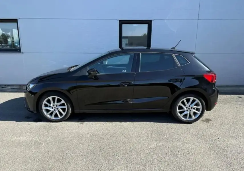 Vue latérale droite d'une SEAT Ibiza 1.0 TSI 95 FR noire, avec jantes alliage et vitres teintées, stationnée devant un mur gris.