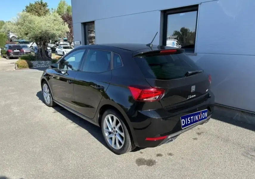 Vue 3/4 arrière droite d'une SEAT Ibiza noire garée devant un bâtiment avec jantes alliage visibles.