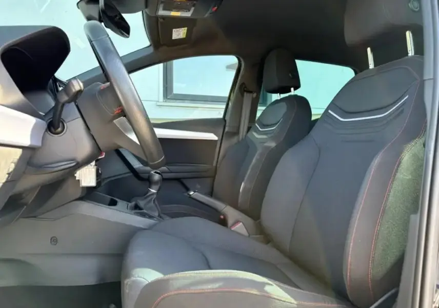 Intérieur de la SEAT Ibiza 1.0 TSI 95 FR 2025, vue côté conducteur montrant sièges noirs avec surpiqûres rouges.