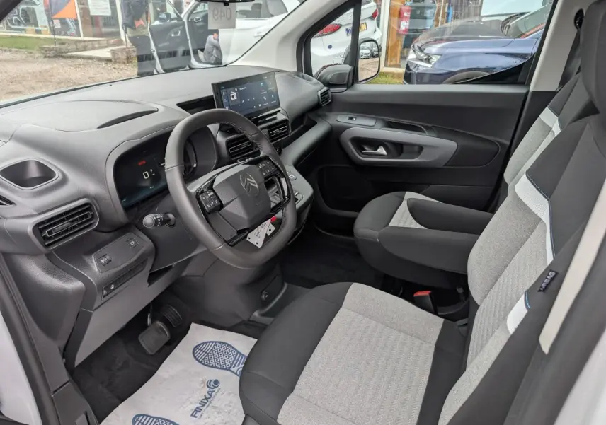 Vue intérieure côté conducteur du Citroën Berlingo blanc 2025, volant cuir multifonctions et sièges tissu bicolores.