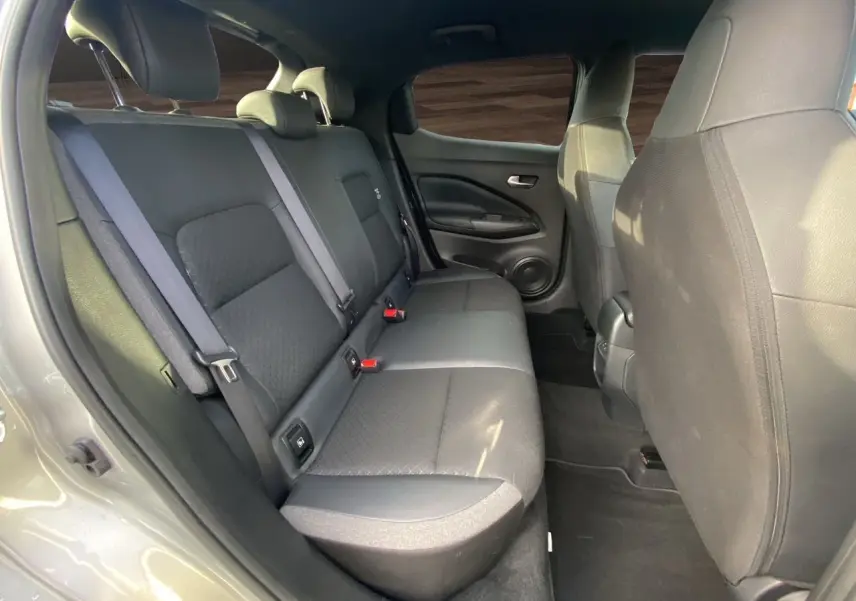 Vue intérieure arrière côté droit du Nissan Juke 2025 gris perle, montrant la banquette tissu noir et les ceintures de sécurité.