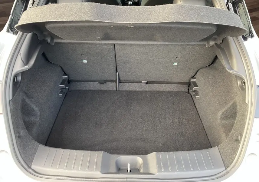 Coffre ouvert vu de l'arrière d'un Nissan Juke 2025 gris perle avec intérieur de coffre noir.