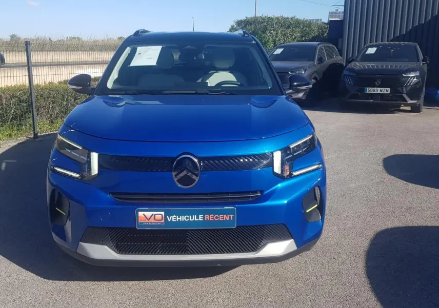 Vue de face d'une Citroën C3 bleu foncé 2024 avec barres de toit et feux LED distinctifs, stationnée en extérieur.