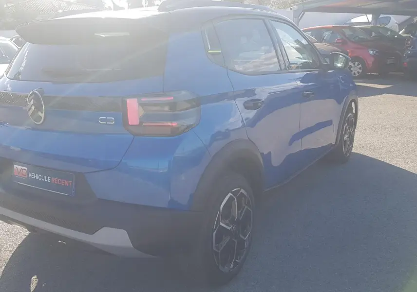 Vue 3/4 arrière droite d'une Citroën C3 bleu foncé 2024 avec jantes alliage et barres de toit visibles.