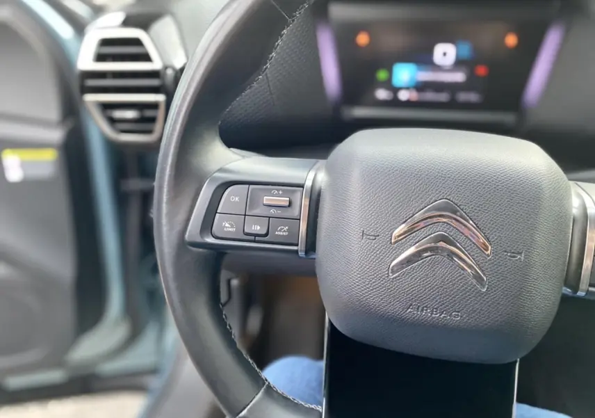 Gros plan sur le volant noir de la Citroën C4 2021, avec commandes intégrées et tableau de bord flou en arrière-plan.